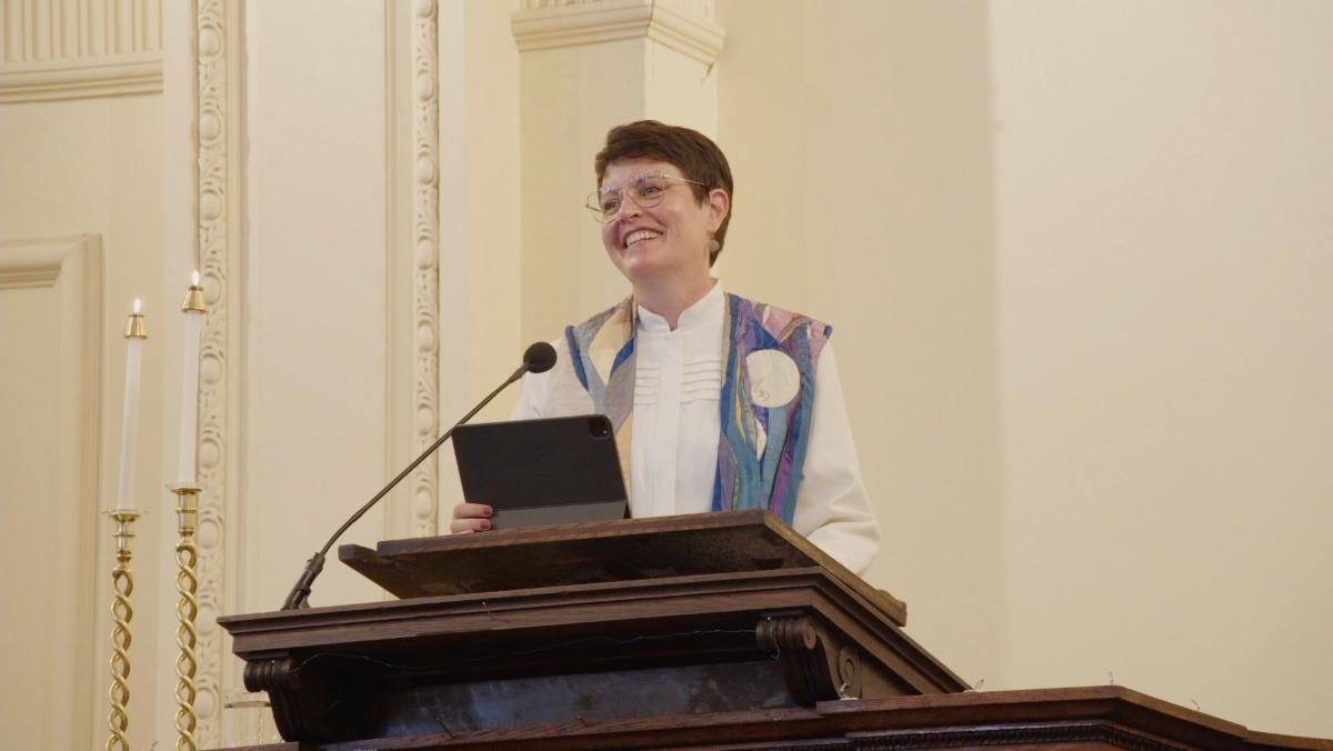 A picture of Rev. Parisa standing at the pulpit and smiling.